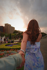woman wearing blue, white, and purple floral dress turning back holding hand of another person in front of camera thumbnail