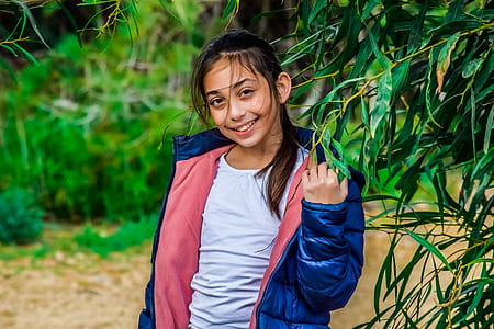 girl wearing blue and pink jacket standing near tree thumbnail