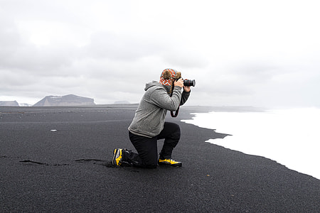 person in gray fleece hoodie on seashore taking a photo while facing the sea thumbnail