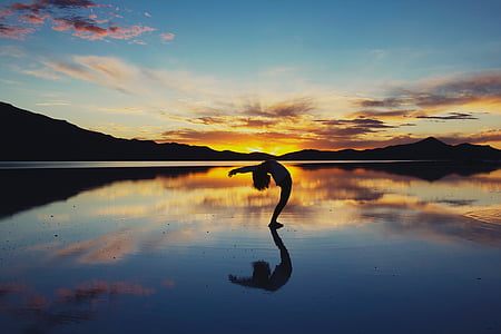 silhouette photo of person bending on body of water against orange sky thumbnail