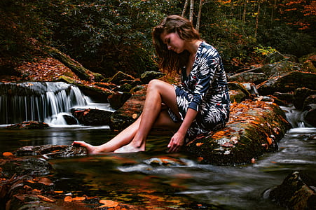 woman sitting on brown stone while her feet on river thumbnail