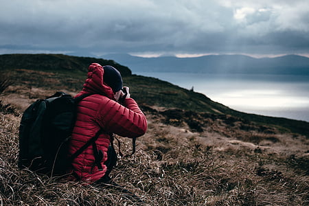 selective focus photography of person sitting on grass captured hill under white clouds and blue sky thumbnail