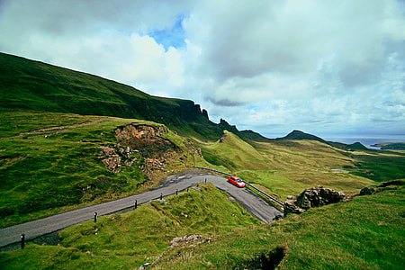 red car on road between green grass field thumbnail