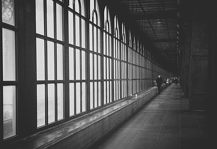 grayscale photo of man walking on hallway near glass window thumbnail