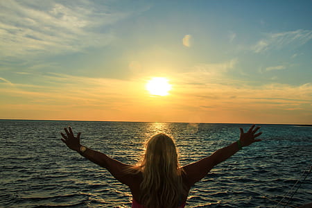 woman raising hands facing ocean thumbnail
