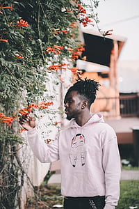 man wearing white pullover hoodie staring and holding orange petaled flower at daytime thumbnail