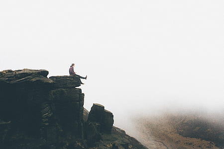 person sitting on rock formation under fog during daytime thumbnail
