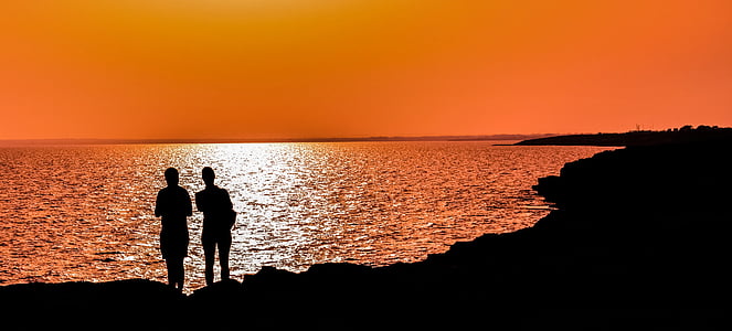 silhouette of two person standing near body of water thumbnail