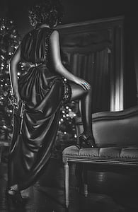 woman in black dress right foot on sofa hiding gun behind her back photo thumbnail