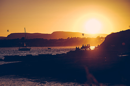 group of people sitting beside body of water near mountain during golden hour thumbnail