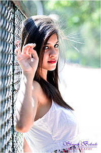 woman wearing white sleeveless top leaning on chain link barrier thumbnail