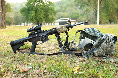 black assault rifle with scope beside gray tactical vest on green grass field photo thumbnail