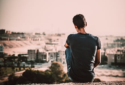 Man in Black Shirt and Blue Denim Jeans Sitting on Gray Stone at Daytime thumbnail