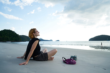 woman wearing black shirt and shorts sitting on seashore watching sea thumbnail