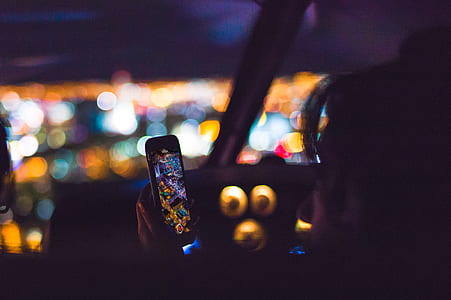bokeh photography of person sitting on vehicle passenger seat holding turned on smartphone thumbnail