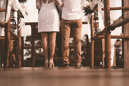 woman and man standing in front of table wearing wedding dresses thumbnail