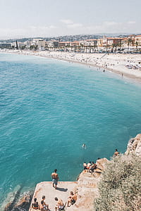blue water white sand beach with lots of people during day thumbnail