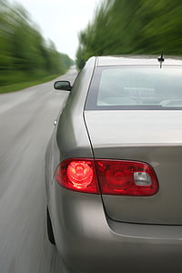 gray vehicle passing on road between trees thumbnail