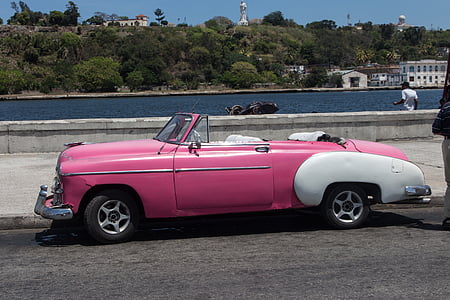 pink convertible coupe parked beside body of water thumbnail