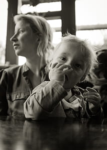grayscale photography of child sitting on lap of her mother in front of the table thumbnail