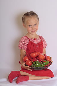 smiling girl sitting on white textile carrying vegetable basket with assorted vegetables thumbnail