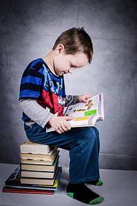 boy reading book sitting on stack of books thumbnail