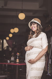 pregnant woman wearing white striped long-sleeved dress holding tummy and smiling thumbnail