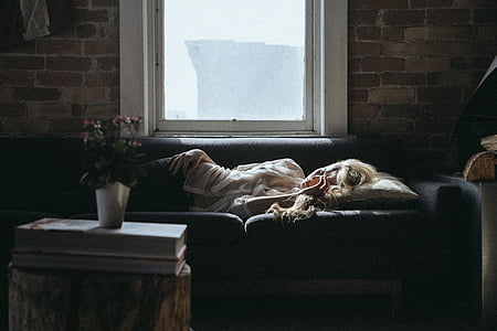 woman in white shirt sleeping on black couch near glass window with white frame during daytime thumbnail