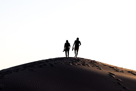 silhouette of two persons walking on desert sand thumbnail