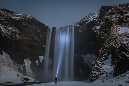 man pointing flashlight toward waterfalls thumbnail
