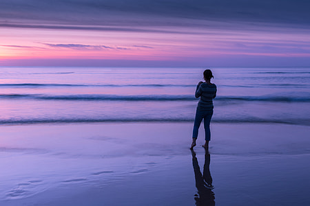 A woman looks out to sea at sunset on a beach in Cornwall, England. This image was captured using a Canon 6D DSLR thumbnail