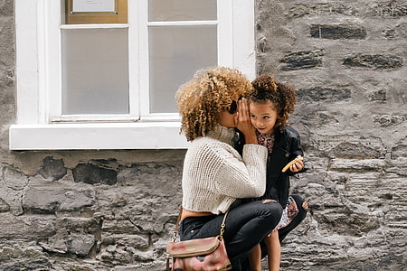 woman whispering girl near white window thumbnail