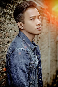 man wearing blue denim button-up jacket beside brown brick wall thumbnail