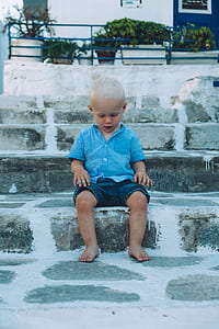 boy in blue button-up t-shirt and blue denim shorts sitting on concrete stairs thumbnail