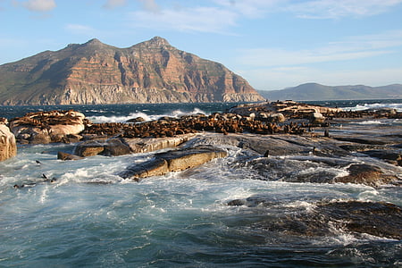 body of water on gray concrete rocks near brown mountain under blue and white sky thumbnail