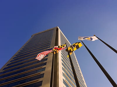 low-angle photography of four flags near building under blue sky thumbnail