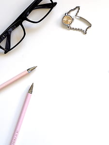 two pink ball-point pens near black framed eyeglasses on white surface thumbnail