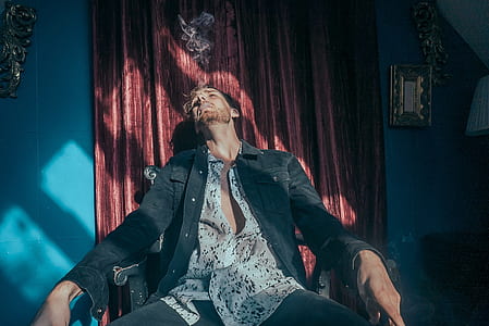 man sitting on rocking armchair near red curtain thumbnail