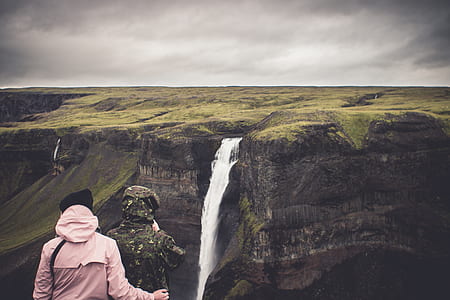 two people in front of waterfalls under cloudy sky during daytime thumbnail