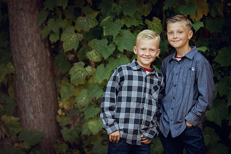 two boys standing against green trees thumbnail