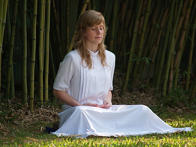 woman wearing white dress sitting on green grass with eyes closed during daytime thumbnail