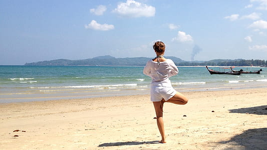 woman standing by one foot on beige sand near body of water during daytime thumbnail