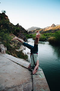 man turning upside down near river and rocky mountain during daytime thumbnail