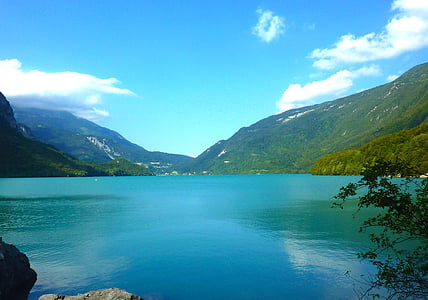 calm body of water beside mountains under blue sky thumbnail