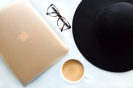 silver MacBook near eye glasses, sun hat  and caramel coffee served on white ceramic mug thumbnail