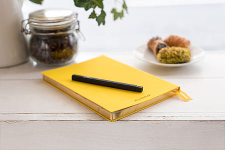 black pen on top of yellow book near jar and saucer thumbnail