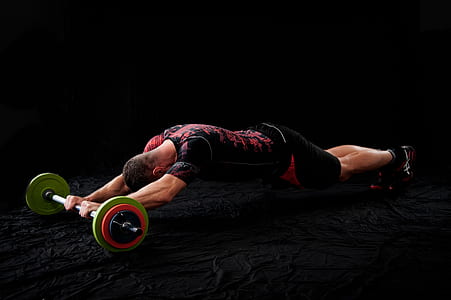 man doing an exercise using barbell while in plank position on black surface thumbnail