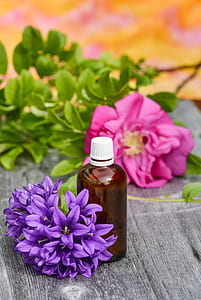 amber glass bottle on grey surface beside purple campanulas and pink peonies closeup photography thumbnail