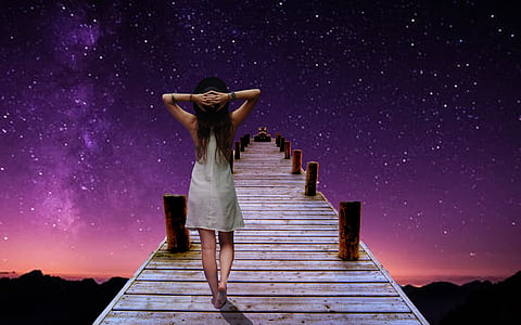 woman holding the back of her head while walking on dock during nighttime thumbnail