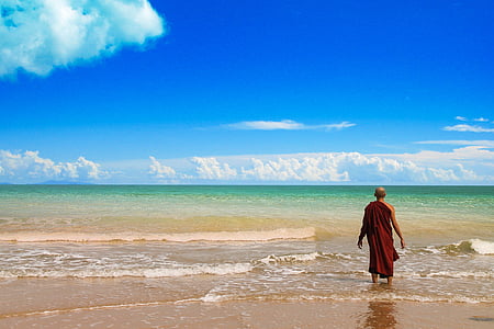 man in red robe standing on beach shore during day time thumbnail